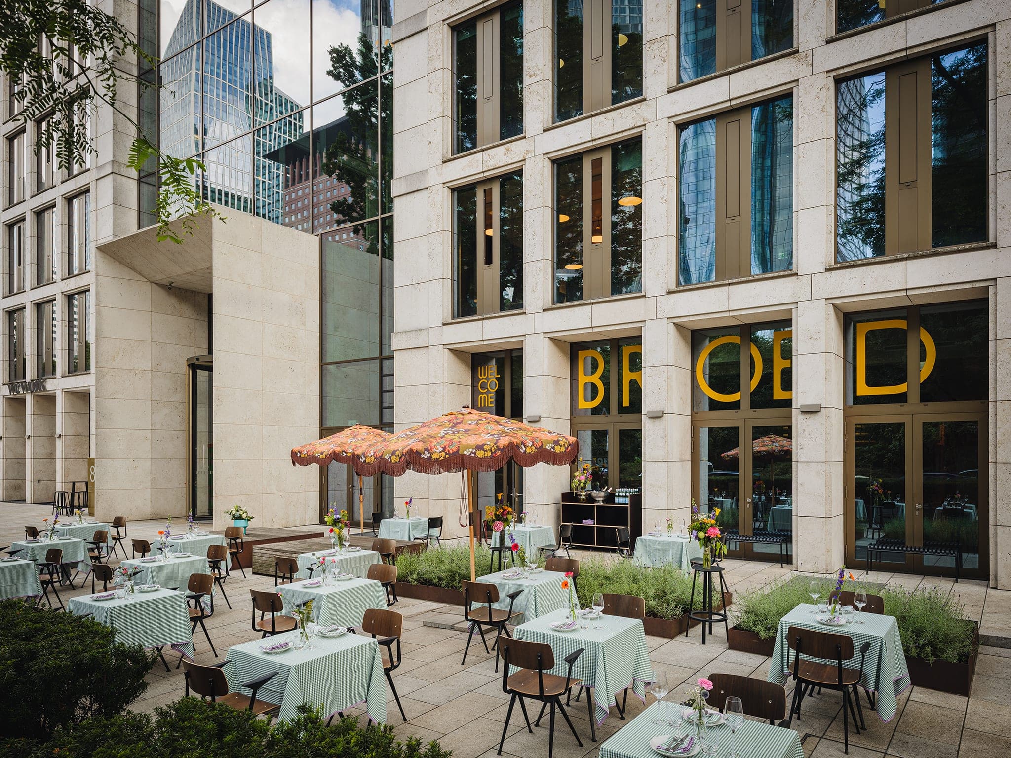 Terrasse mit Schirmen und gedeckten Tischen vor der BROED-Fassade